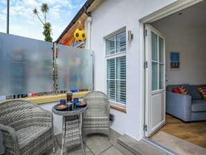 Eine Terrasse mit Korbmöbeln, eine Glastür zu einem Innenraum und Blick zum Himmel.