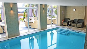 Una piscina interna con pareti in vetro trasparente, mobili in vimini e vista sull'esterno.