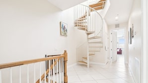A modern staircase with a wooden handrail and white railings, leading to a room with white tiled flooring and a door at the end. - Waterfront 4-level Townhome with Rooftop Deck! (Clearwater Beach)