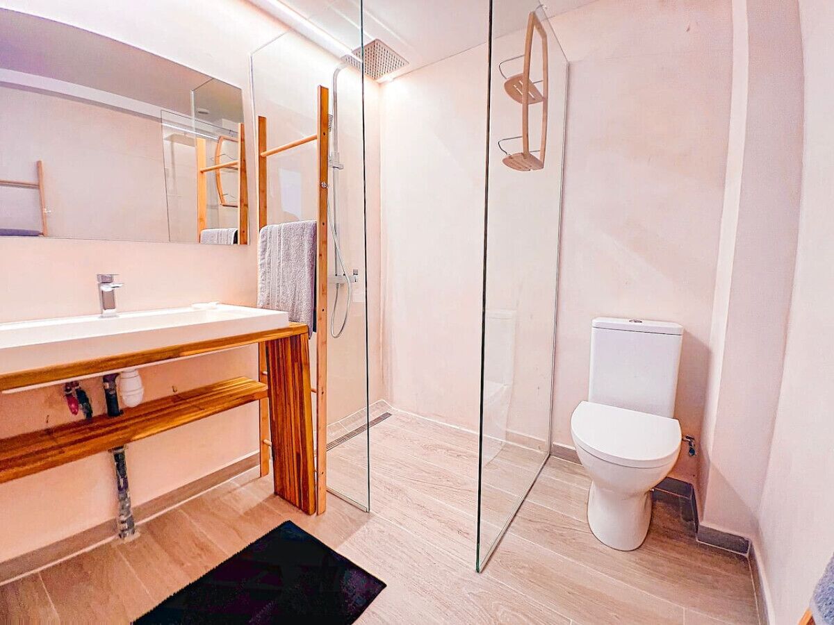 Une salle de bain moderne avec une douche à parois de verre, un meuble-lavabo en bois et des toilettes blanches.