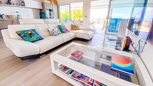 Een moderne woonkamer met een witte bank, kleurrijke kussens, een glazen salontafel en uitzicht op de omgeving.