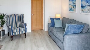 A living room with a striped armchair, a grey sofa, a wooden door, and two wall-mounted lamps. - 2 bedroom accommodation in Sandyhills (Sandyhills)