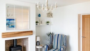 A room with a fireplace, a striped armchair, a small table with a lamp, and a wooden door. - 2 bedroom accommodation in Sandyhills (Sandyhills)