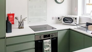 A kitchen with a stove, microwave, and a clock on the wall. - 2 bedroom accommodation in Sandyhills (Sandyhills)