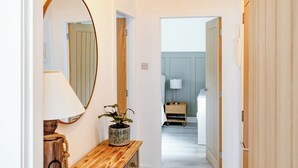 A hallway with a wooden bench, a mirror, a potted plant, and a door leading to a bedroom with a bedside table and lamp. - 2 bedroom accommodation in Sandyhills (Sandyhills)