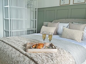 A bed with a textured blanket, a tray with croissants and glasses of wine, and a white shelving unit. - 2 bedroom accommodation in Sandyhills (Sandyhills)
