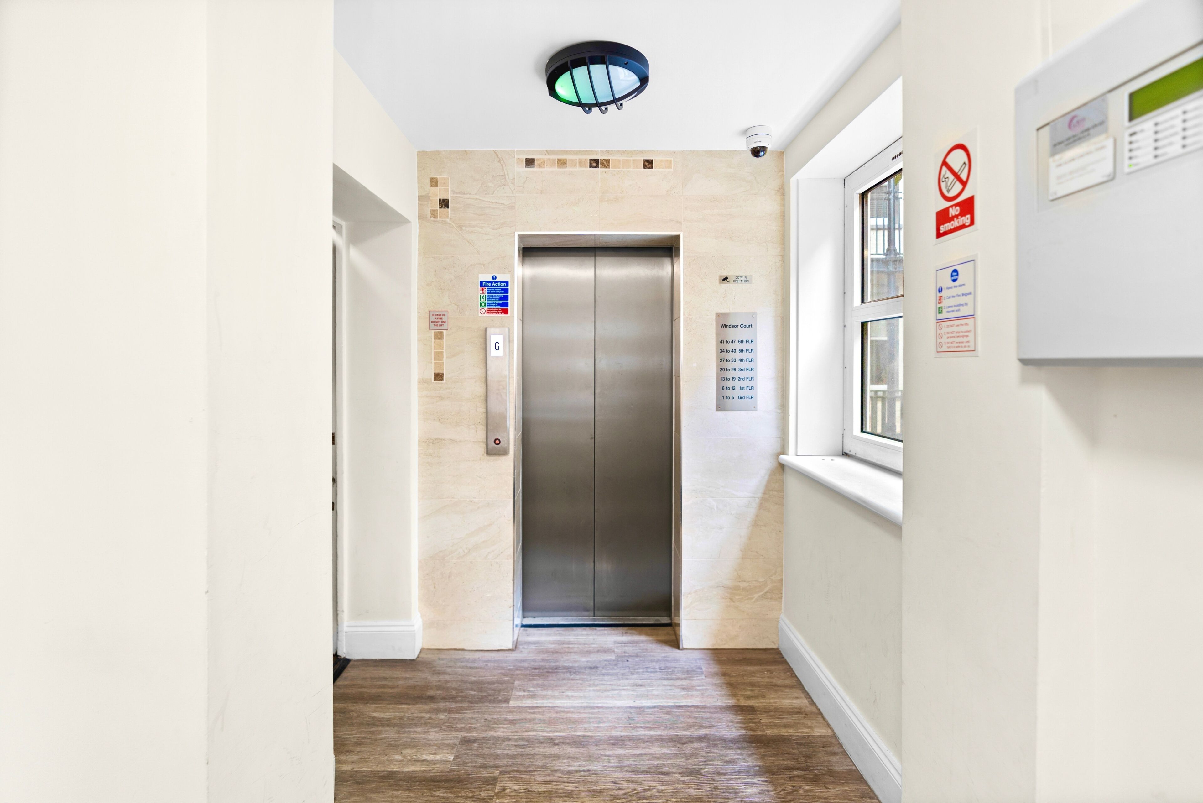 A hallway with a wooden floor, an elevator, and a window.