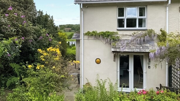 A house with a stone roof, a small garden with various plants and flowers, and a white door. - Lower Axford Cottage (Callington)
