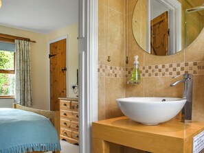 A bathroom with a white sink, a wooden vanity, a mirror, and a shower area. - Lower Axford Cottage (Callington)