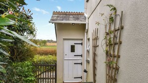 A small, single-story building with a white door and a small porch area. - Lower Axford Cottage (Callington)