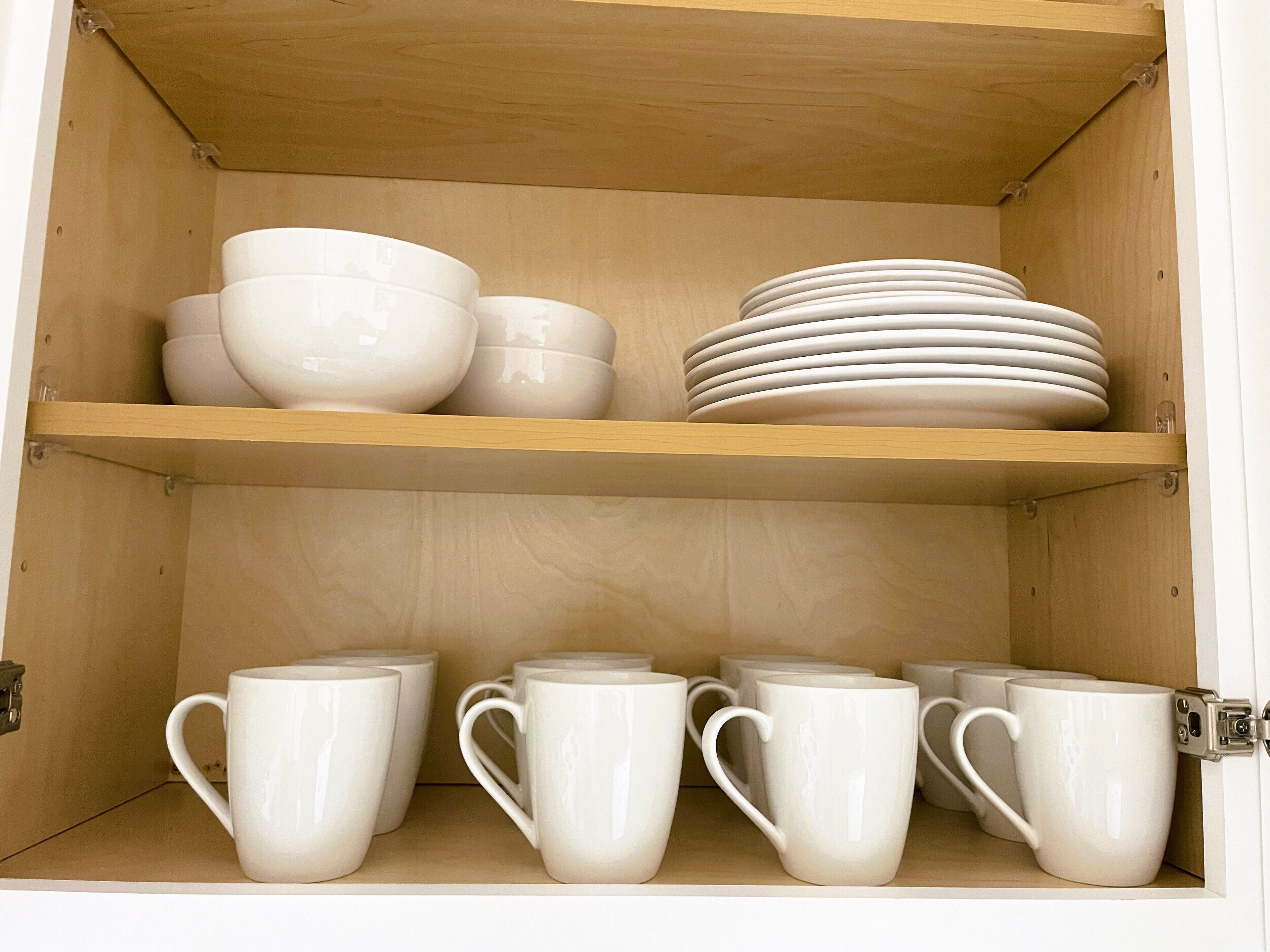 A wooden cabinet with shelves holding white bowls, plates, and mugs.