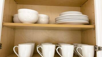 A wooden cabinet with shelves holding white bowls, plates, and mugs.