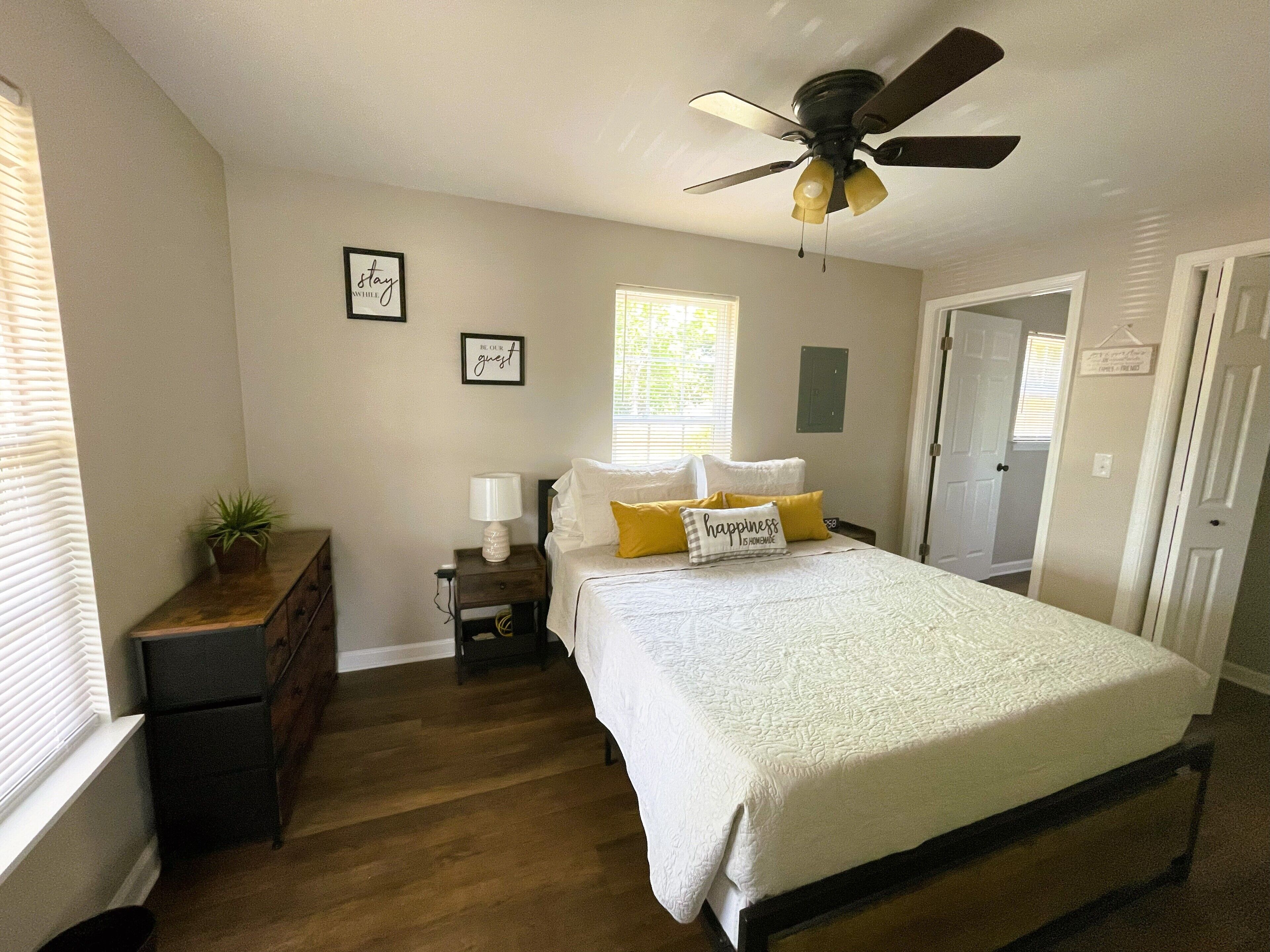 Quarto com cama, mesa de cabeceira, ventoinha de teto e janela.