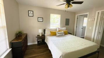 Quarto com cama, mesa de cabeceira, ventoinha de teto e janela.