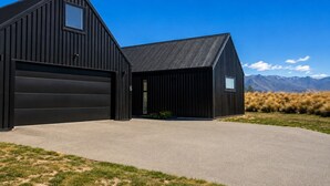 A modern black barn with a garage, a driveway, and a mountainous backdrop. - The Big House, Twizel (Twizel)