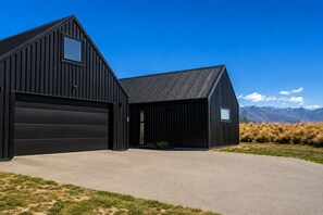 A modern black barn with a garage, a driveway, and a mountainous backdrop. - The Big House, Twizel (Twizel)