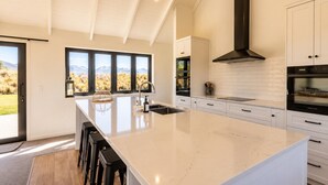 A modern kitchen with a large island, white cabinetry, and a view of the outdoors. - The Big House, Twizel (Twizel)