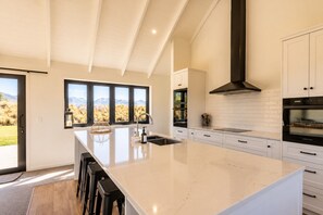 A modern kitchen with a large island, white cabinetry, and a view of the outdoors. - The Big House, Twizel (Twizel)