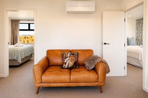 A room with a brown leather sofa, a window with a view of yellow flowers, and a door leading to another room. - The Big House, Twizel (Twizel)
