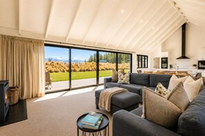 A modern living room with a sofa, a coffee table, and a fireplace. There is a large window offering a view of a grassy field and mountains. - The Big House, Twizel (Twizel)