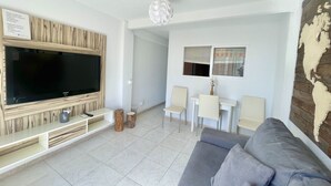 A modern living room with a flat-screen TV, grey sofa, and a small dining area with two chairs and a table. - ALBATROS APARTMENT (R133) (Benidorm)