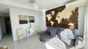 A modern living room with a grey sofa, a small white table with chairs, a world map wall, and a ceiling light fixture. - ALBATROS APARTMENT (R133) (Benidorm)