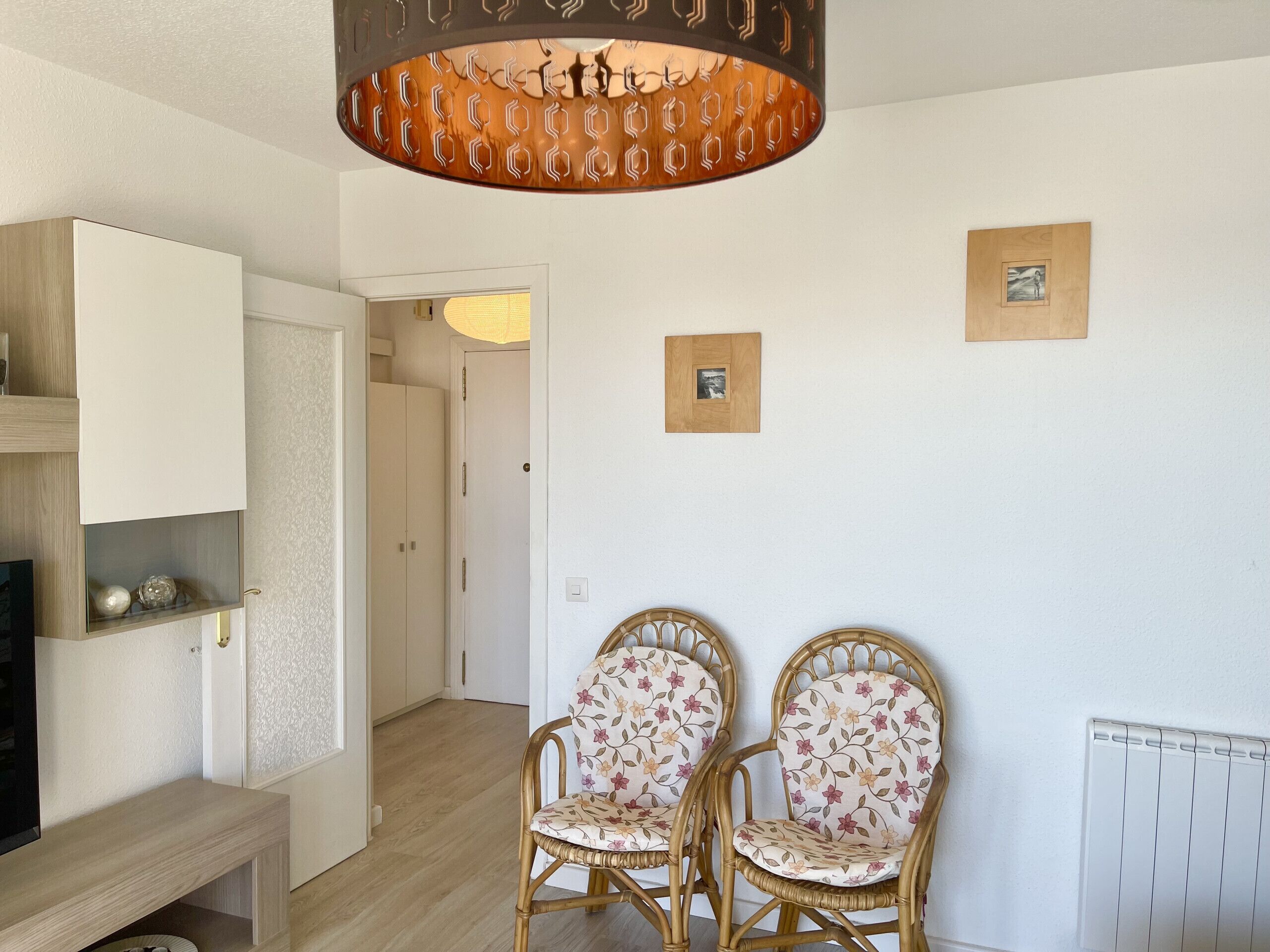 Habitació amb dues cadires de vimet, amb tapisseria floral, un armari de fusta i una làmpada al sostre.