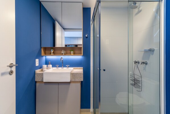 A modern bathroom with a glass shower enclosure, a sink with a countertop, and a mirror above the sink.