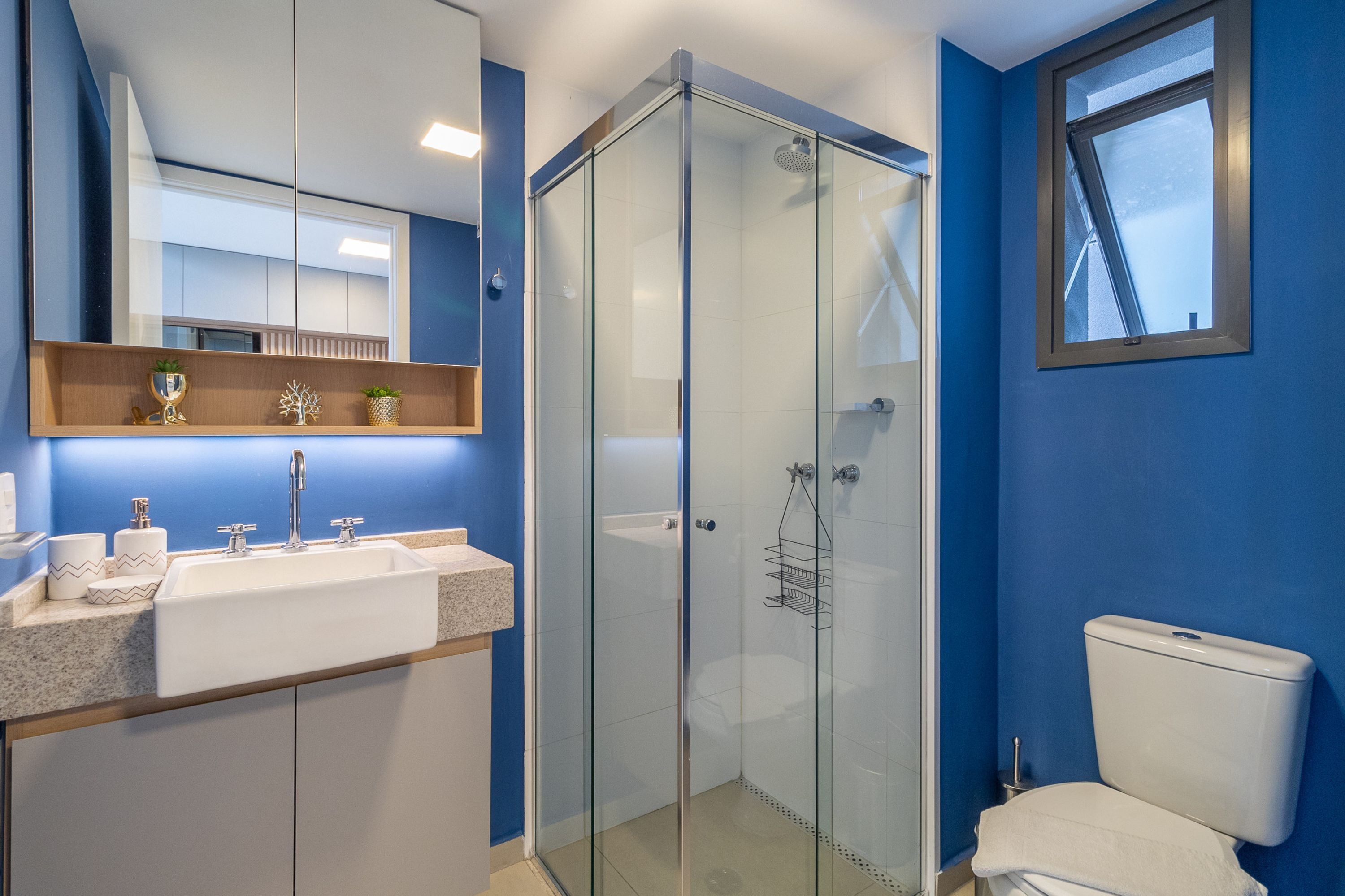 Ein modernes Badezimmer mit einer Glaskabine zur Dusche, einem weißen Waschbecken mit Ablagefläche und einer Toilette.
