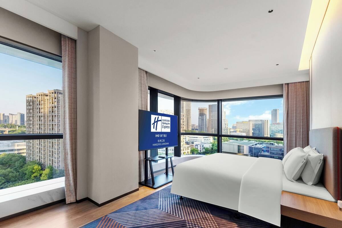 Ein modernes Hotelzimmer mit einem großen Bett, einem Fernseher und Blick auf die Stadt.