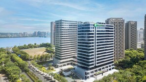 A modern hotel with a prominent Holiday Inn Express sign, surrounded by high-rise buildings and a body of water. - Holiday Inn Express Hangzhou Jiangnan by IHG (Hangzhou)