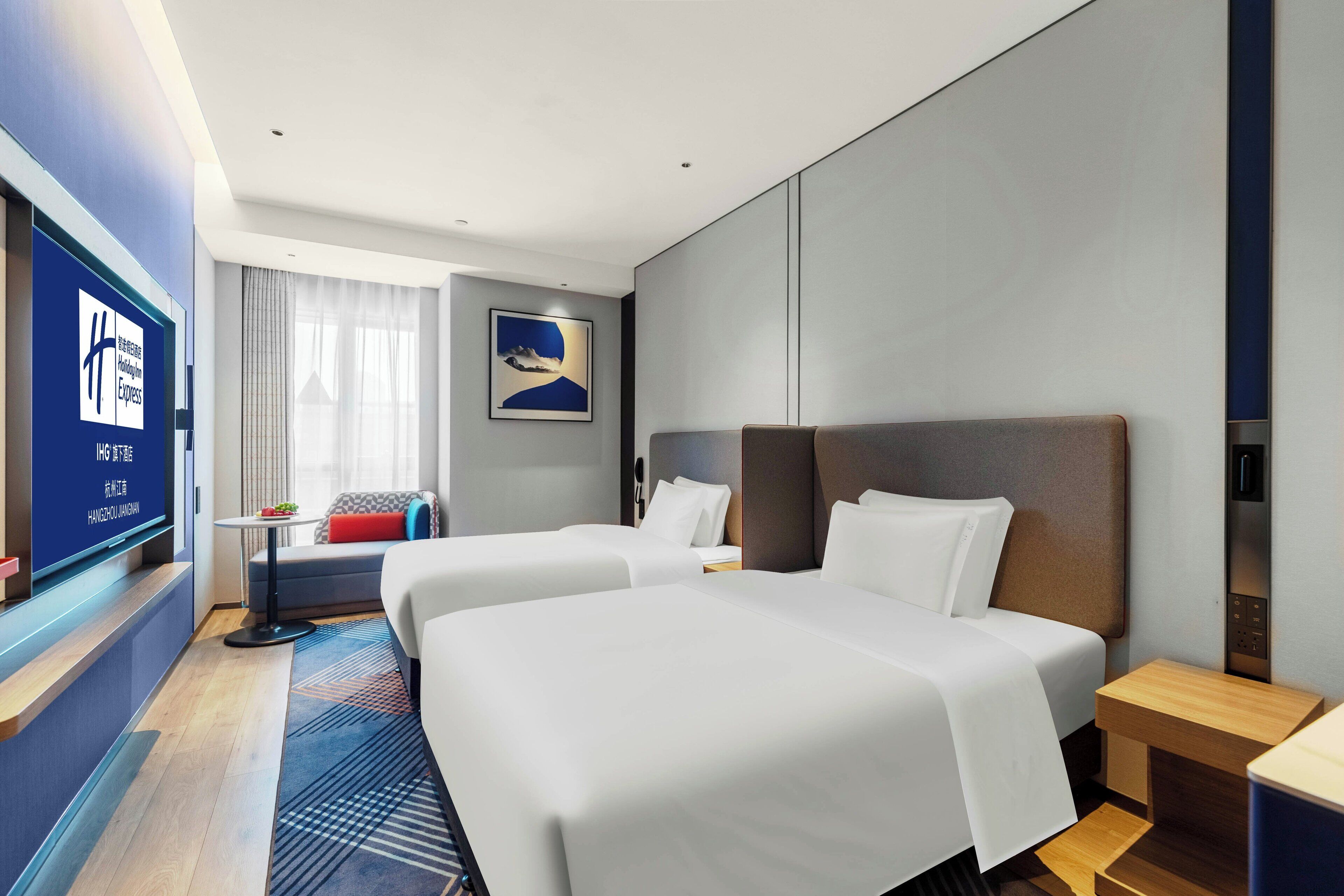 A hotel room with two beds, a TV, a small table, and a window with curtains.