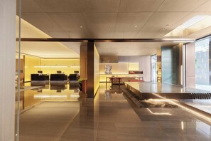 A modern lobby with a reflective floor, a reception desk, a seating area, and a water feature.
