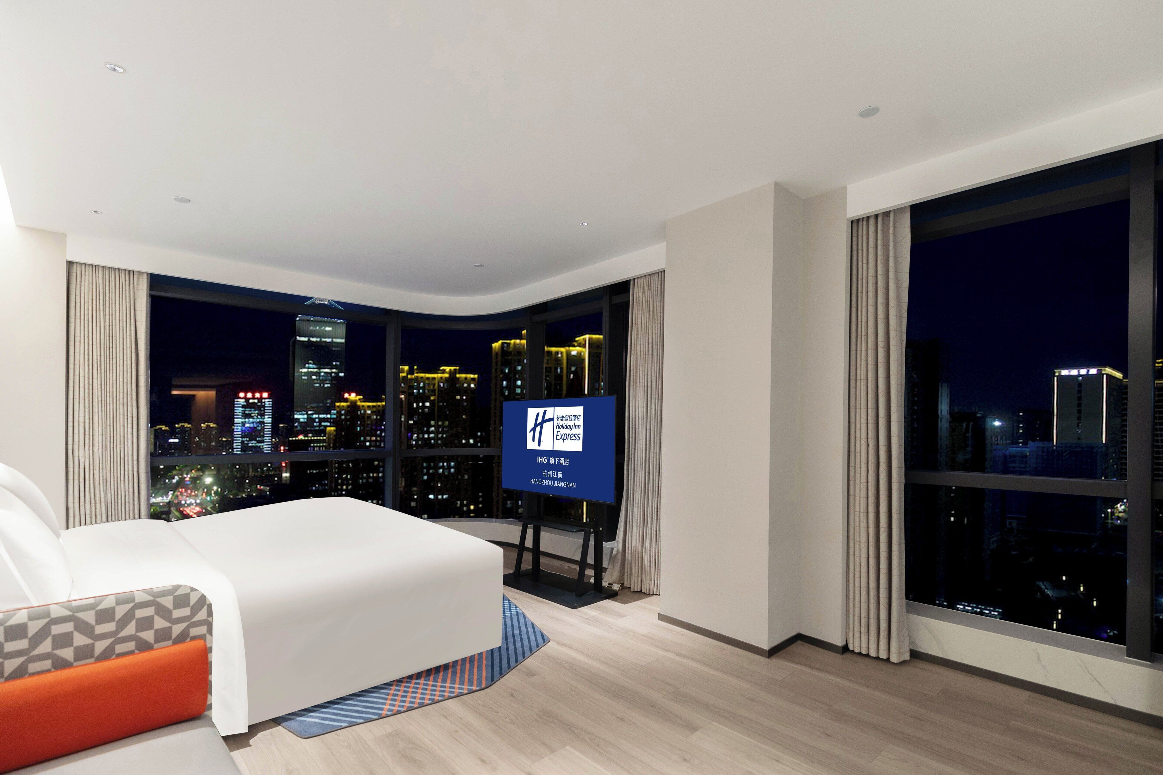 A modern hotel room with a large bed, a city view, and a television on a stand.