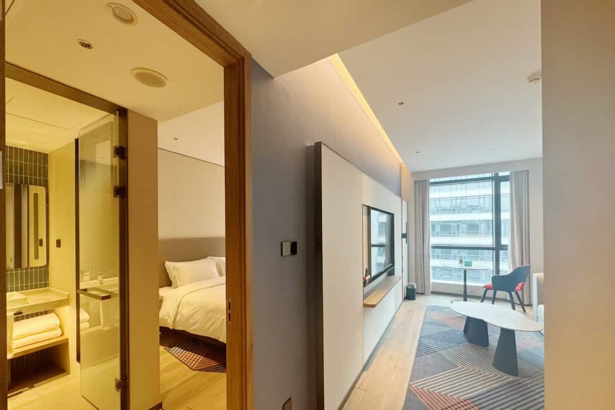 Ein modernes Hotelzimmer mit Bett, Fernseher, Schreibtisch und Blick auf die Stadt durch große Fenster.