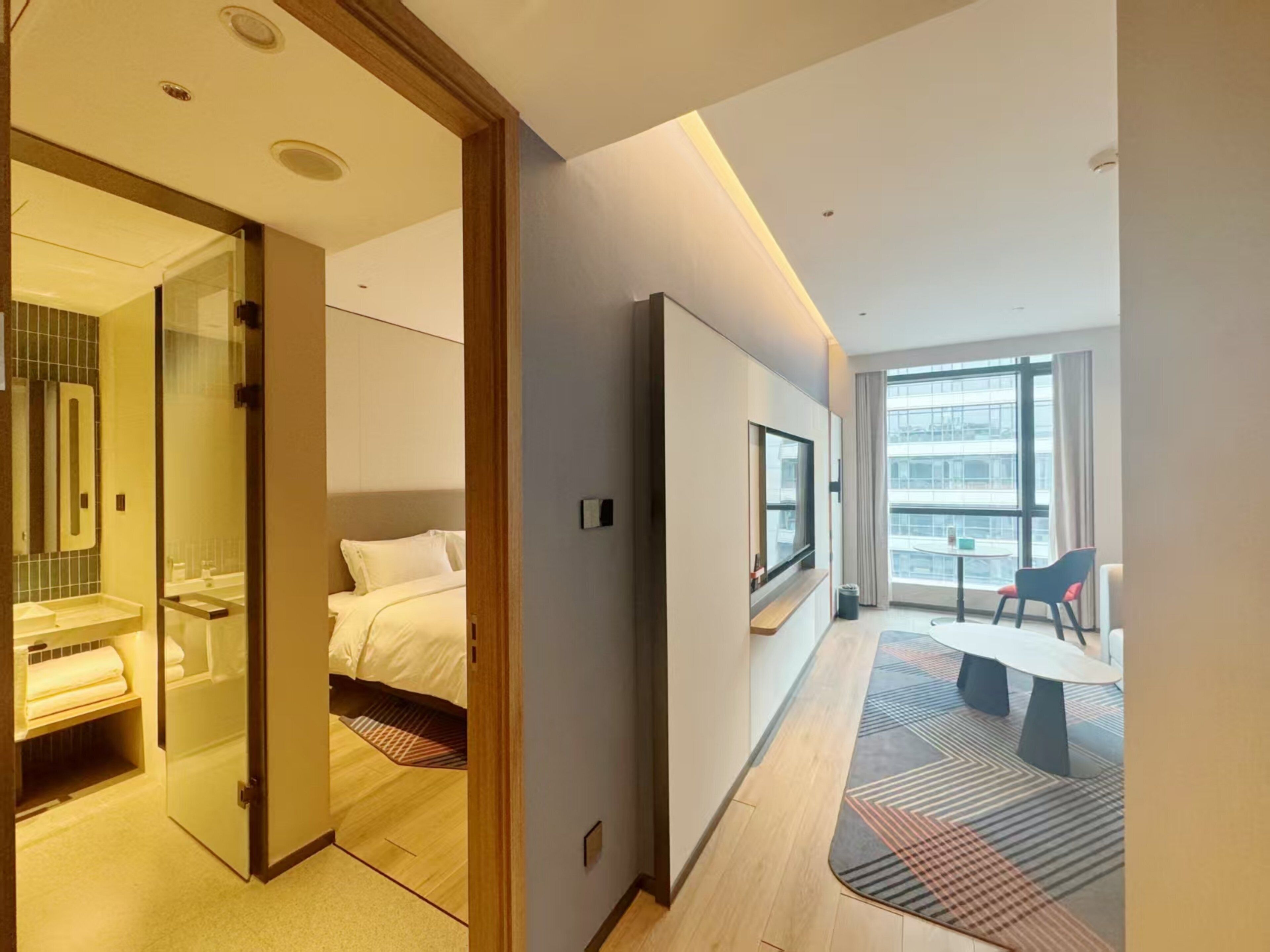 Una camera d'albergo moderna con un letto, una televisione, una scrivania e vista sulla città attraverso ampie finestre.