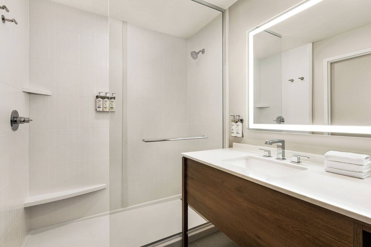Un baño moderno con ducha de vidrio, tocador de madera y un espejo grande.