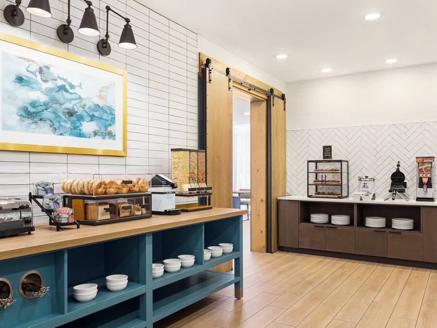 A breakfast buffet area with a variety of food items, a coffee machine, and a large abstract painting on the wall.