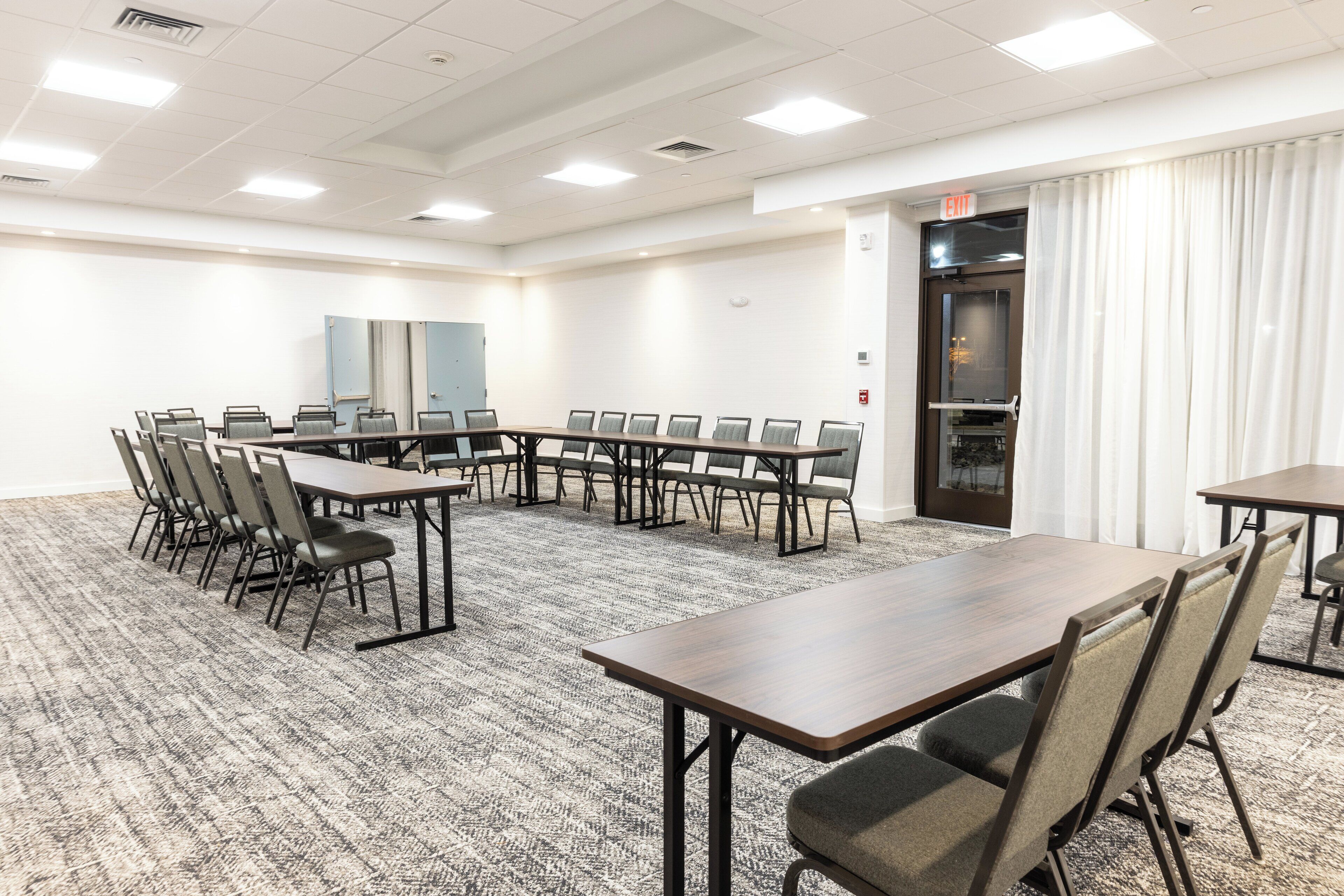 A conference room with a long table and chairs, carpeted floor, white walls, and a door with curtains.