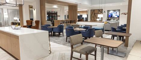 Un hall d’hôtel moderne avec un comptoir d’accueil en marbre, plusieurs espaces de détente et un bar.