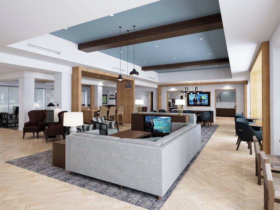 A spacious lobby with a modern design, featuring a large seating area, a reception desk, and a television screen.