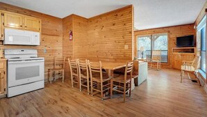 L’intérieur d’un chalet en bois comprend une table et des chaises, un poêle, un four à micro-ondes et un téléviseur.