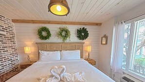 A bedroom with a large bed, two wall-mounted wreaths, two bedside lamps, and a window with blinds. - "Farmhouse Chic: Poolside Luxury" Sleeps 16 (Pigeon Forge)