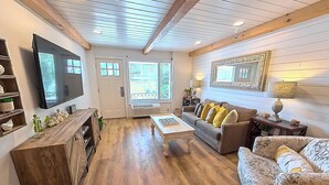 A spacious living room with a wooden floor, a large TV, a sofa with yellow cushions, and a patterned armchair. - "Farmhouse Chic: Poolside Luxury" Sleeps 16 (Pigeon Forge)
