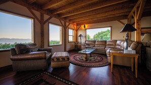 A spacious living room with a wooden ceiling, leather furniture, and large windows offering a view of the outdoors. - Cozy lodge near town w Stunning Views & Fireplace (Homer)