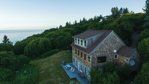 A two-story house with a stone facade, a large deck, and a view of the ocean. - Cozy lodge near town w Stunning Views & Fireplace (Homer)
