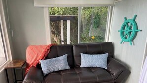Ein braunes Ledersofa mit zwei gemusterten Kissen, einer roten Decke und einem blauen Hocker mit einer Zeitschrift.