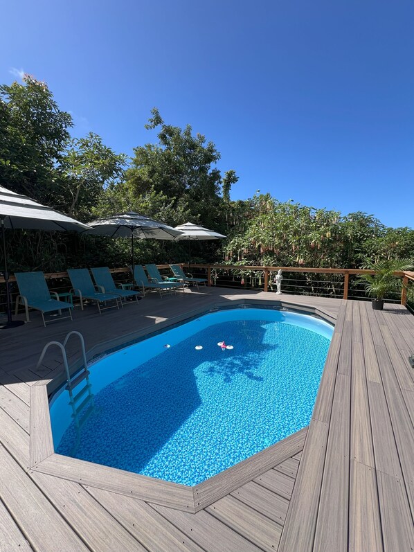 Une piscine entourée d’une terrasse en bois, de chaises longues et de parasols.