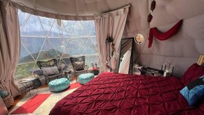 Ein gemütliches Schlafzimmer mit einem großen Bett, Ausblick durch ein Fenster und einer Sitzecke mit Sesseln.
