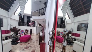 A spacious living area with a high ceiling, a central red pillar, and a view of the upper floor through a glass wall. - Charming House, Convenient Location in Bucaramanga (Bucaramanga)